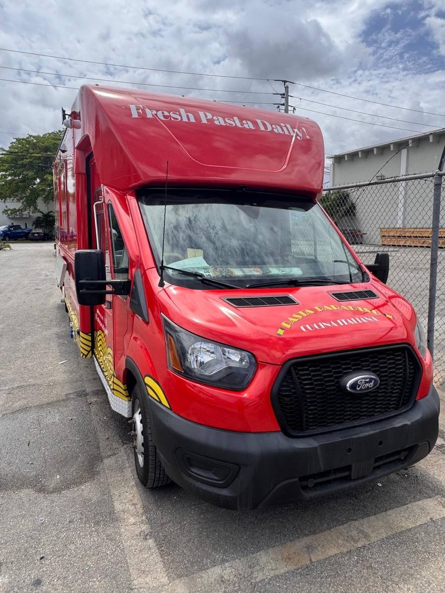 Front three-quarter view of the Pasta Paradiso food truck, a red Ford Transit with 'Fresh Pasta Daily!' painted above the windshield.