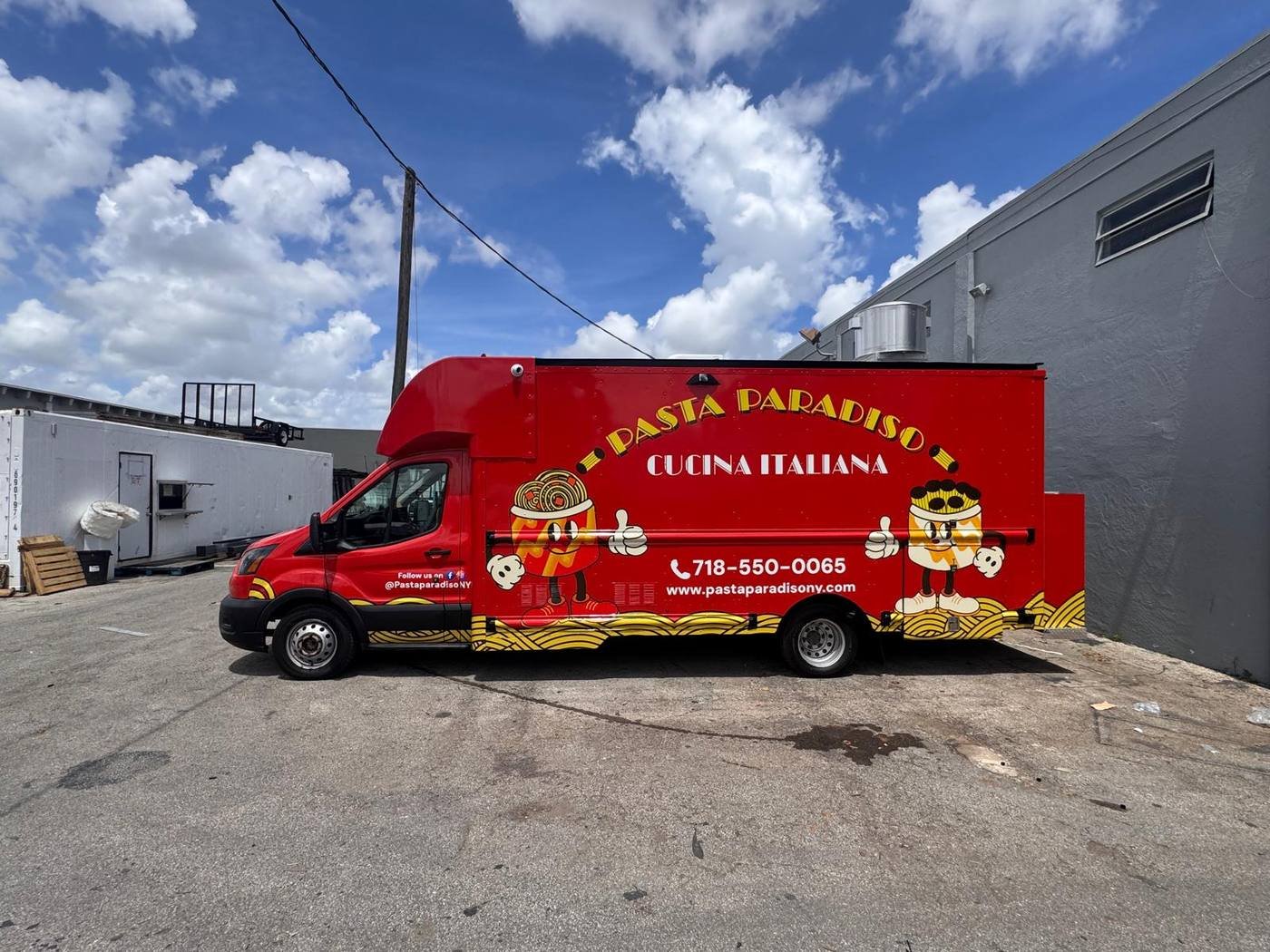 The red Pasta Paradiso food truck, wrapped in illustrated pasta-swirl graphics and the Pasty mascot, parked in a New York City lot.